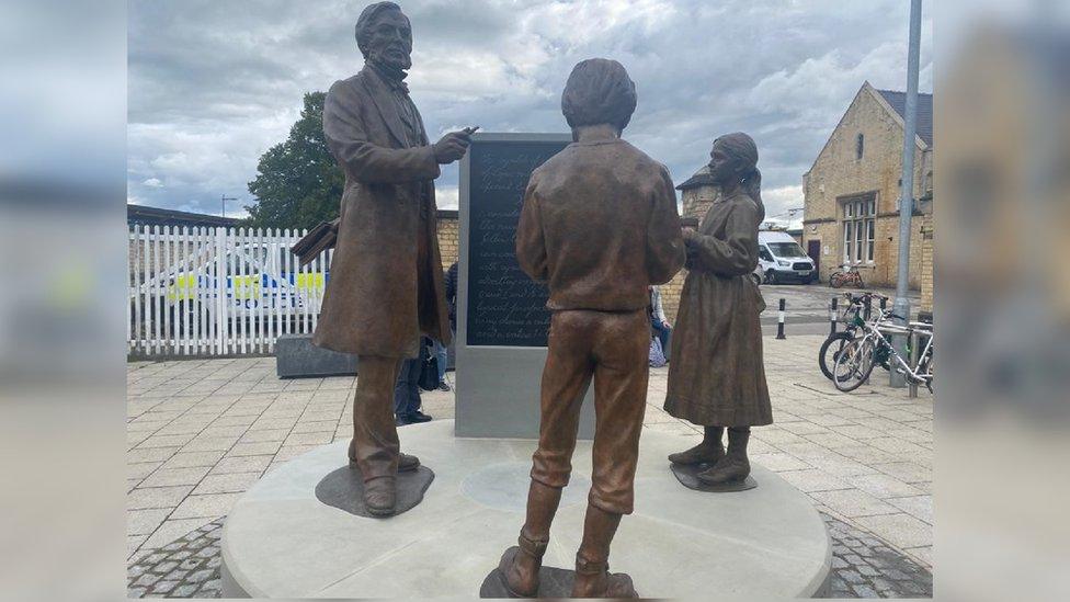 The bronze artwork depicts a larger than life-size Boole teaching a boy and girl at a blackboard