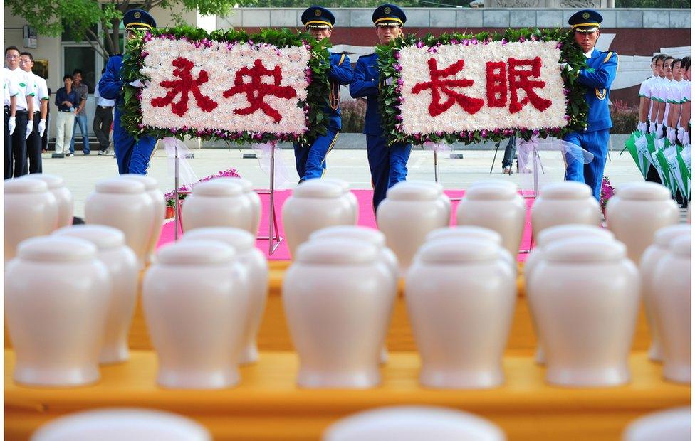 Attendants approach a table filled with biodegradable urns while carrying a floral display with characters meaning 'rest in peace forever' during a procession at a cemetery in Tianjin, northern China, for a collective eco-burial on 20 July 2010