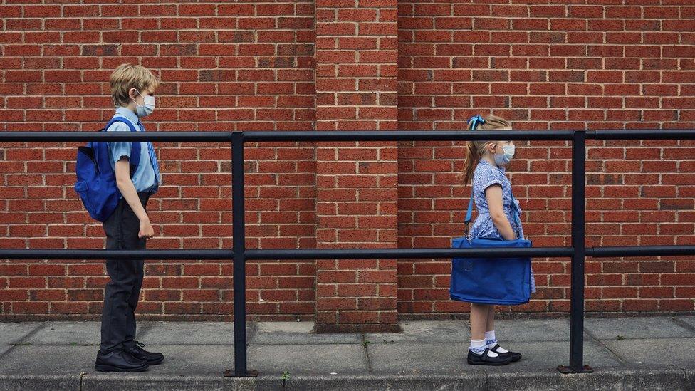 Two schoolchildren wear masks to school.