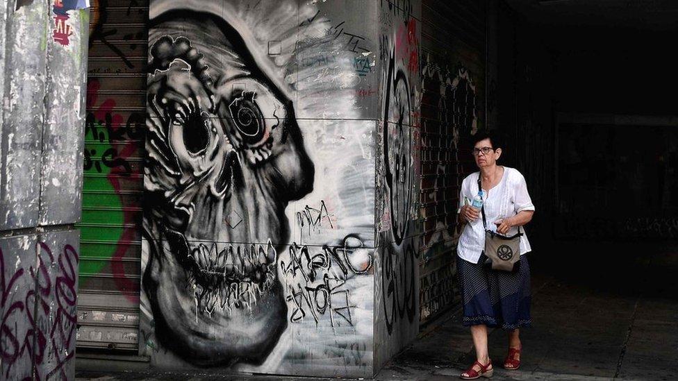 A woman walks past a vandalised Greek Manpower Employment Organisation building in central Athens, 9 August 2018