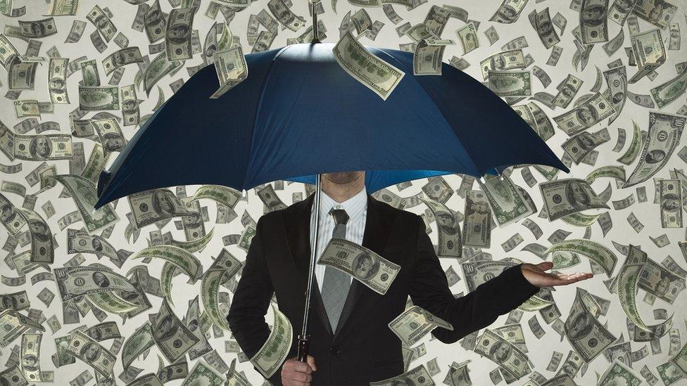 Person stood beneath an umbrella and lots of money