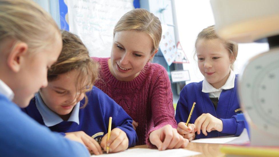 A teacher sits at a desk working with a number of young primary school pupils