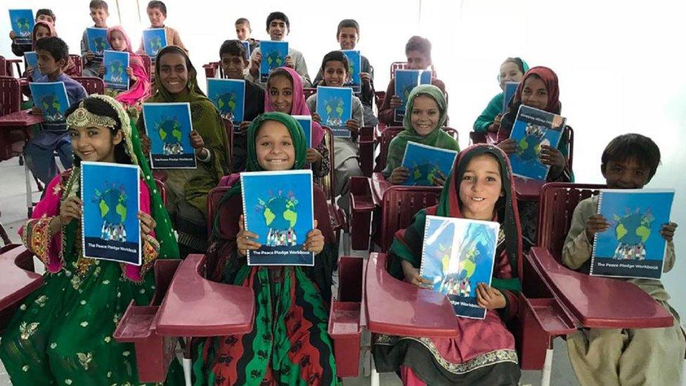 A-group-of-seated-school-children-holding-up-peace-brochures.