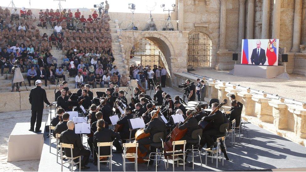 Russian President Vladimir Putin (on screen, R) delivers a speech via live video feed during a concert by the Mariinsky Theater Orchestra in Palmyra amphitheatre in Tadmur District, Homs Governorate, Syria, 05 May 2016