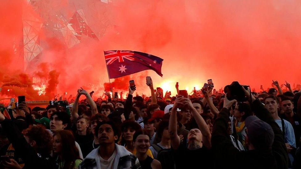 An Australian flag flies with a red smoke background