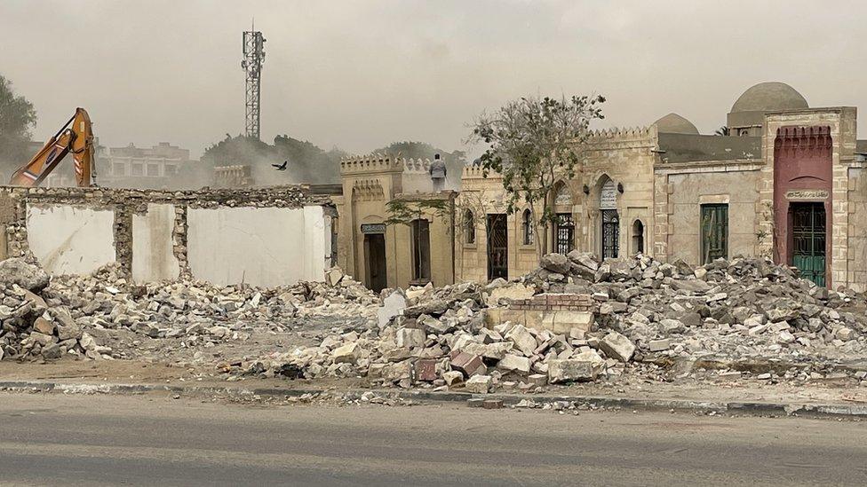 Demolition under way with bulldozer seen in the background, men on roof of tomb in Sayyida Nafisa cemetery