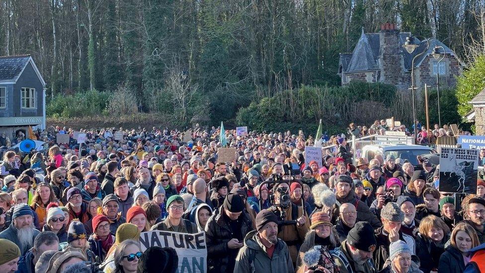 Crowd of people stand in the middle of a square holding signs and banners