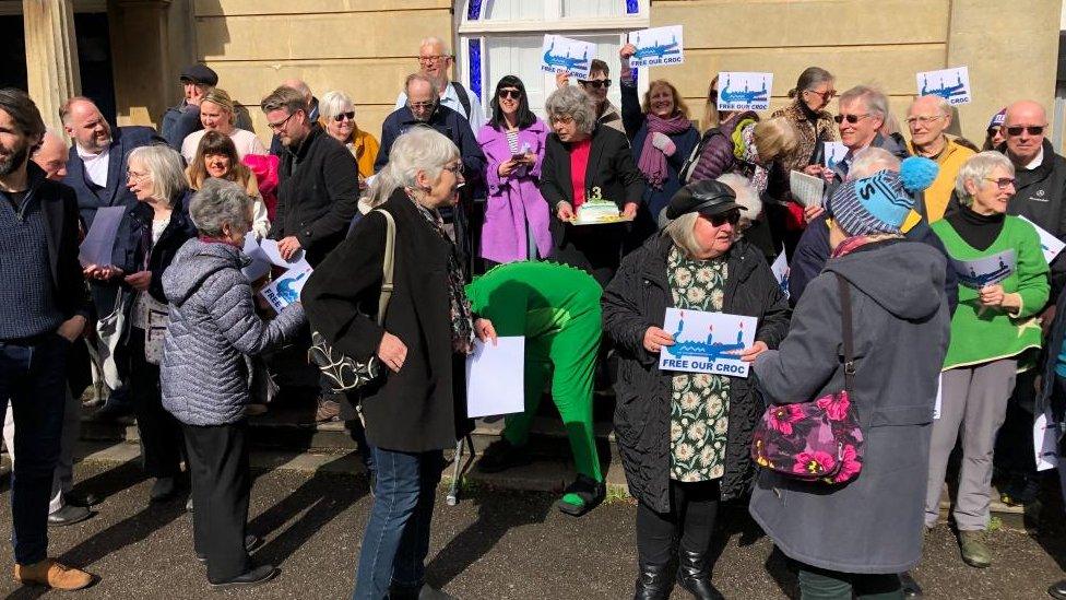 A crowd of people holding "free our croc" signs