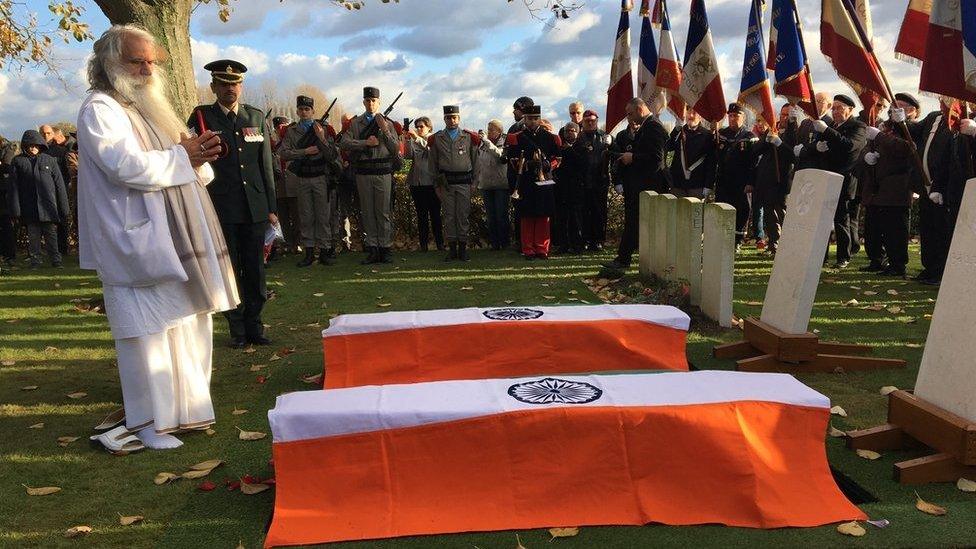 A Hindu priest chants in front of two coffins draped with the Indian flag