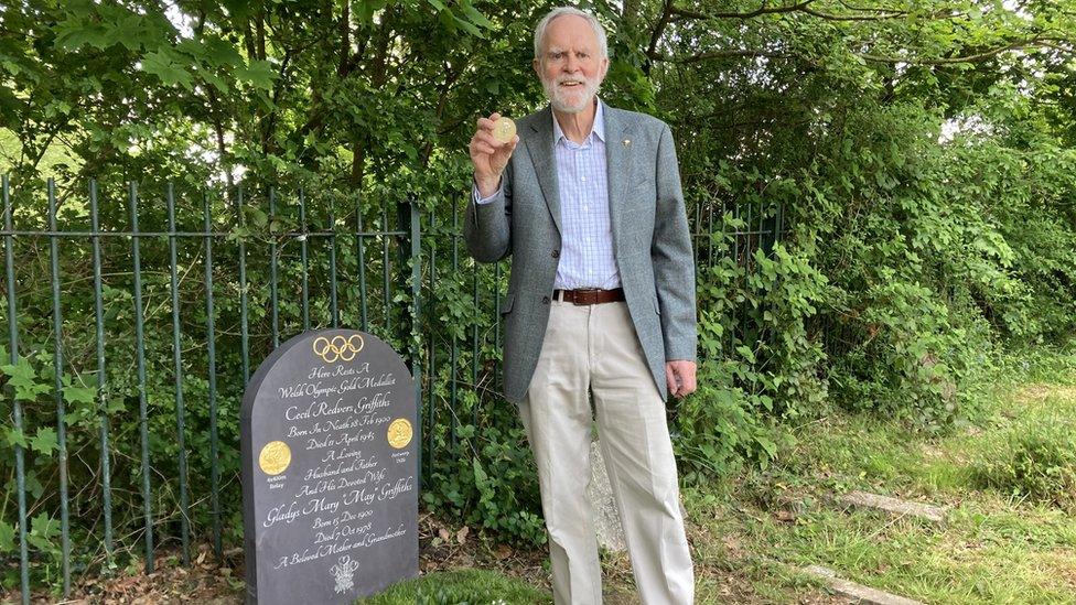 John standing by the headstone and holding the Olympic medal