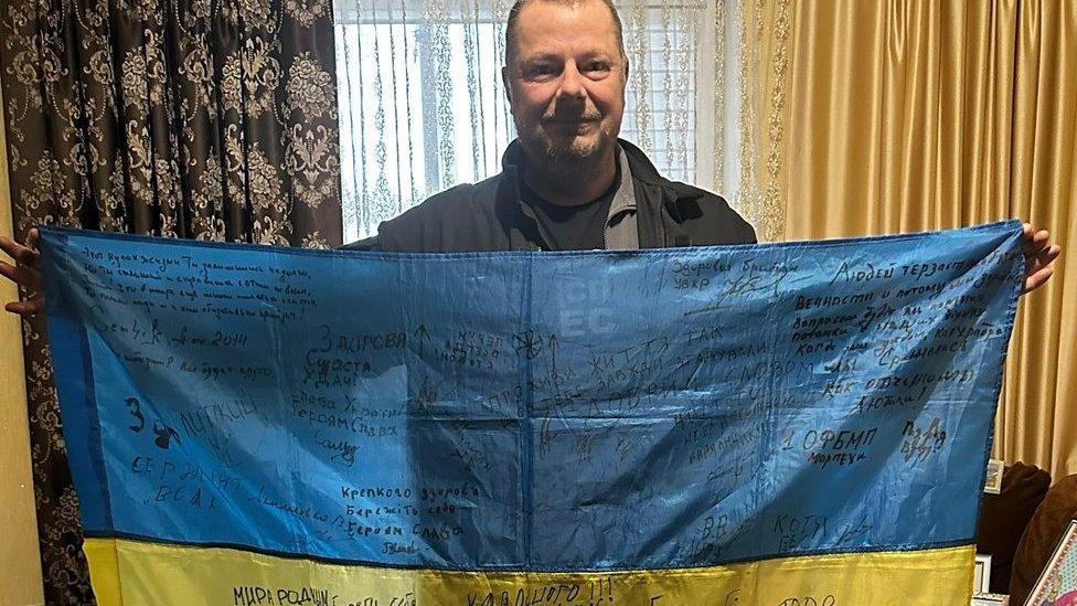 Elliott Svatos holding a Ukrainian flag covered in signatures