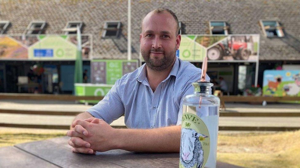 Bryn Perry sitting on a bench with a bottle of his gin