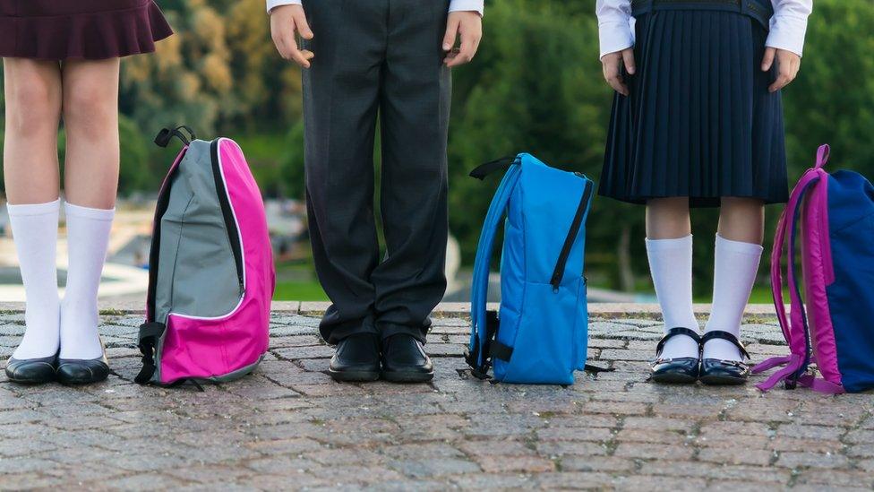 generic image of three children standing beside school bags