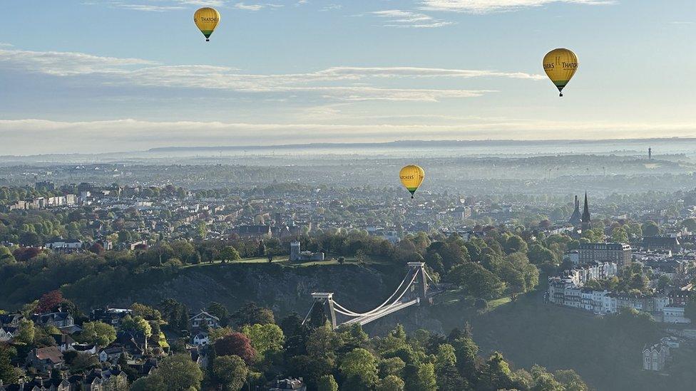 Three hot air balloons over Bristol with the Clifton Suspension Bridge in the foreground on a sunny day