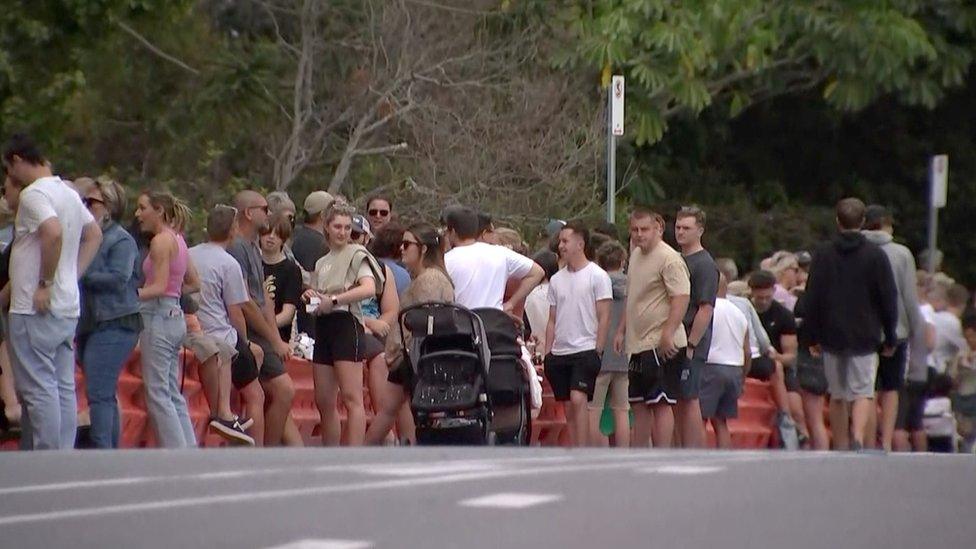 Dozens of people line a barricade on a road to make the state border