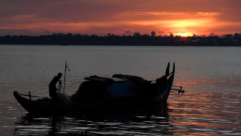 A fisherman sorts out a net on a boat in the Mekong River in Phnom Penh, June 2022