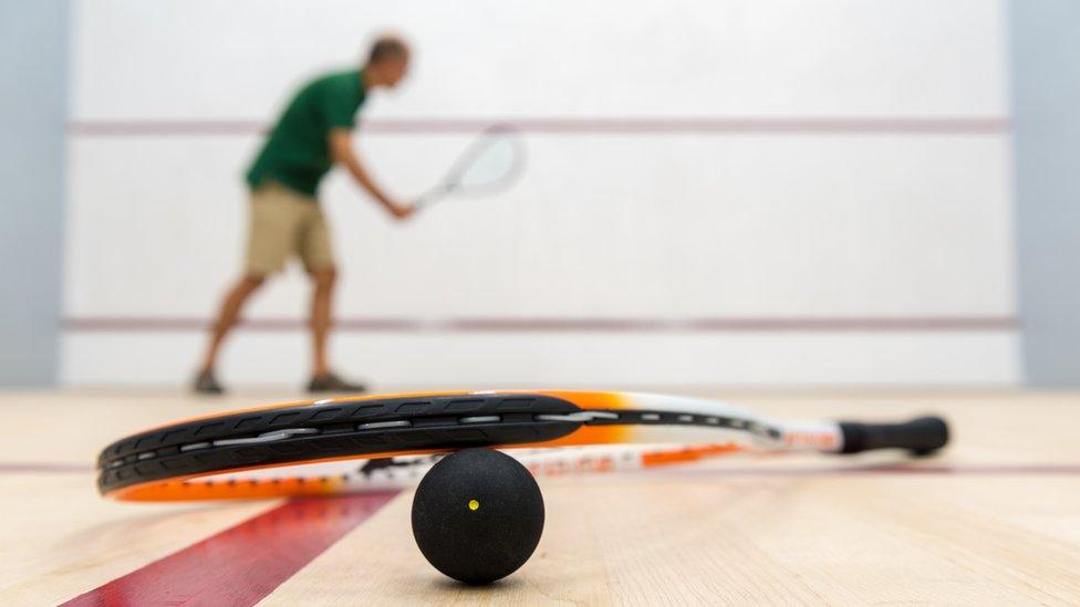 Squash player, racket and 1-spot ball lying on the floor of an empty squash court