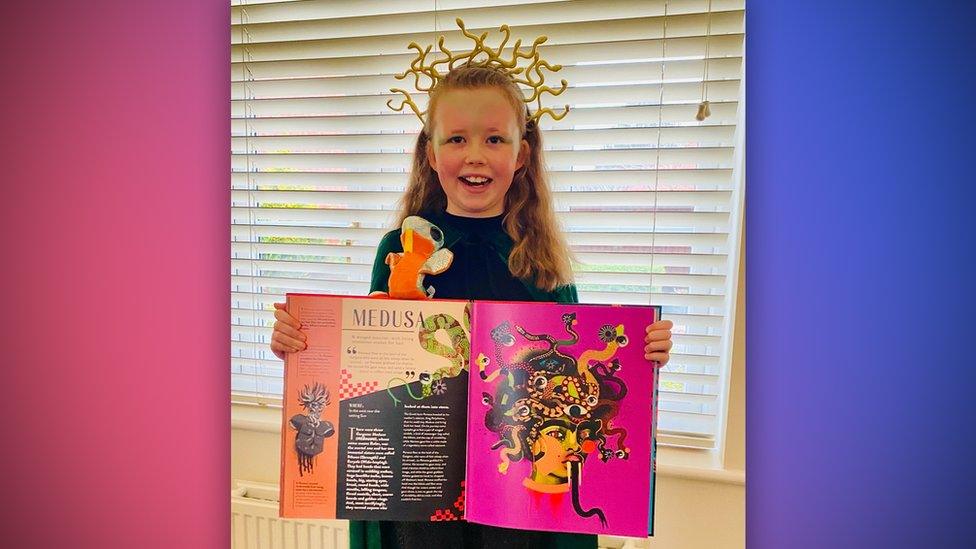girl dressed up with snakes on her head and holding a book open with a story about medusa