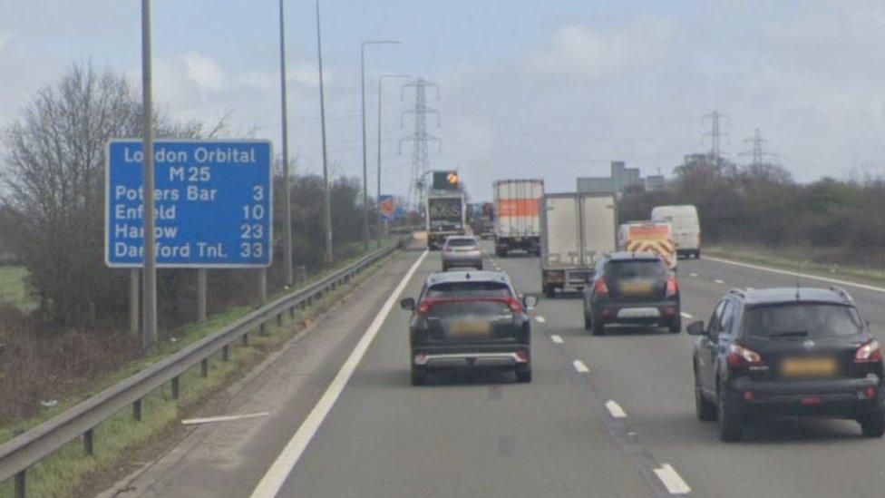 M25 between junctions 23 and 25. You can see traffic across four lanes and a blue motorway sign showing the number of miles to various locations including Potters Bar and Harlow.