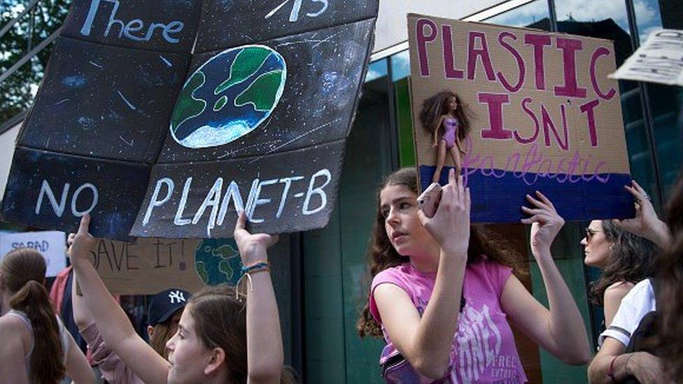 Girls hold up homemade posters that read "there is no planet b" and "plastic isn't fantastic" alongside an image of Barbie