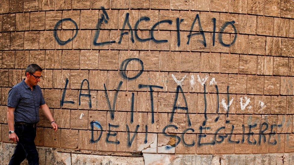 A man in Taranto, Italy, walks past graffiti reading: "Steel or life, you have to choose." It is a reference to the high-polluting Ilva steel plant in Taranto, 27 April 2018