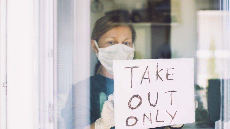 woman wearing a mask putting up take out only sign in shop