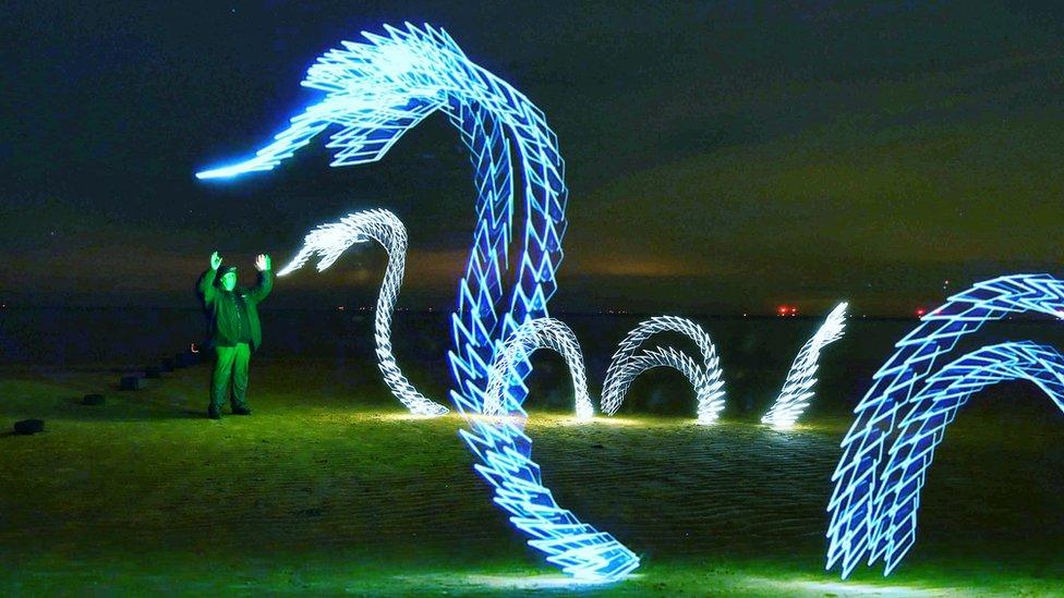 Kevin Jay's light image of two blue-coloured serpents, with a man standing in front of them