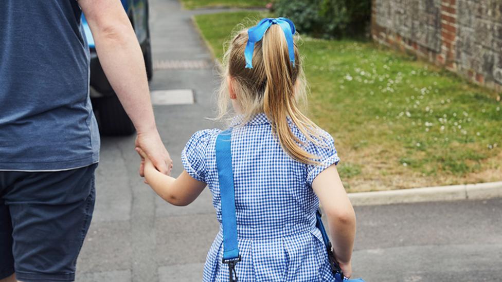 Stock image of a father and daughter walking to school