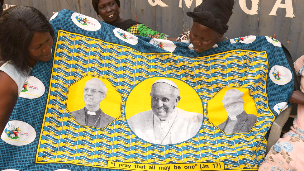 Women hold a printed fabric showing the portrait of the three visiting clerics, Juba, South Sudan - 30 January 2023