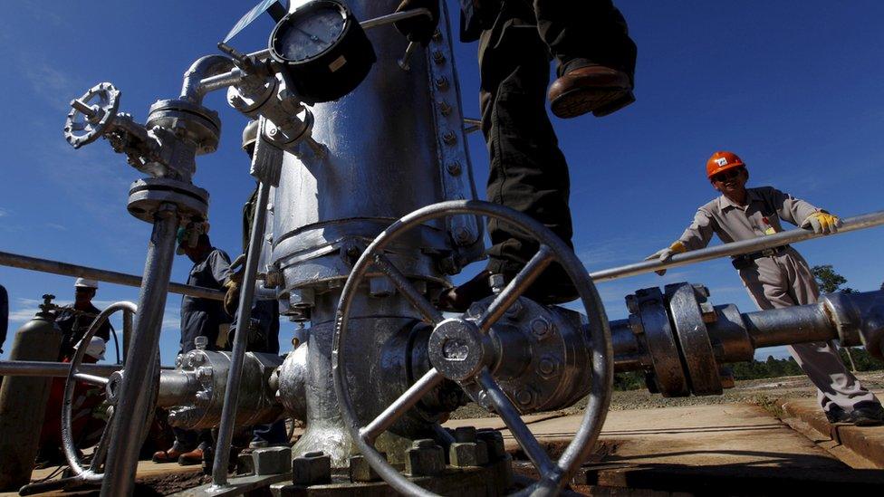 A worker climbing on a gauge at a crude oil well