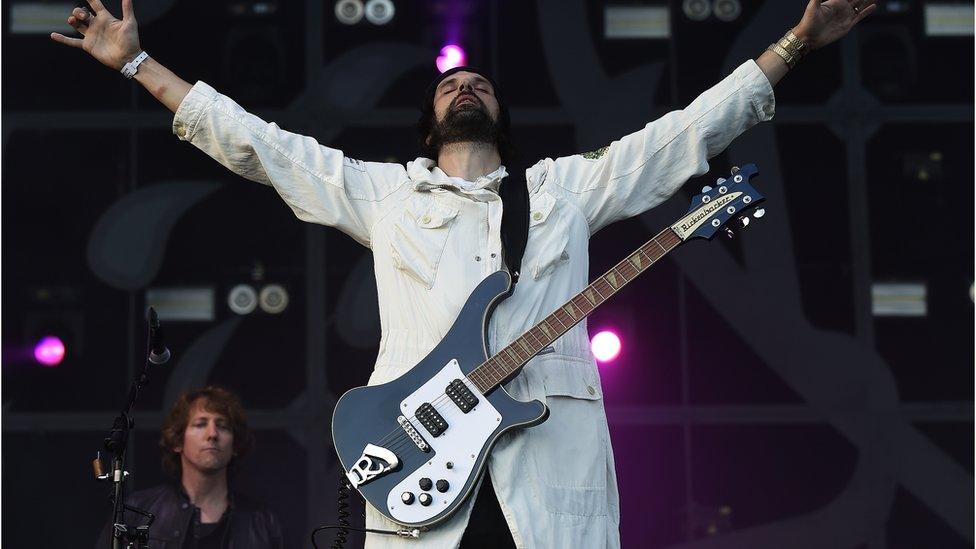 Serge from Kasabian performs on stage with his arms held out to his side