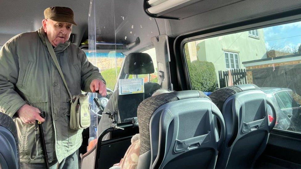 Man wearing a cap and a raincoat walks down the aisle of a bus