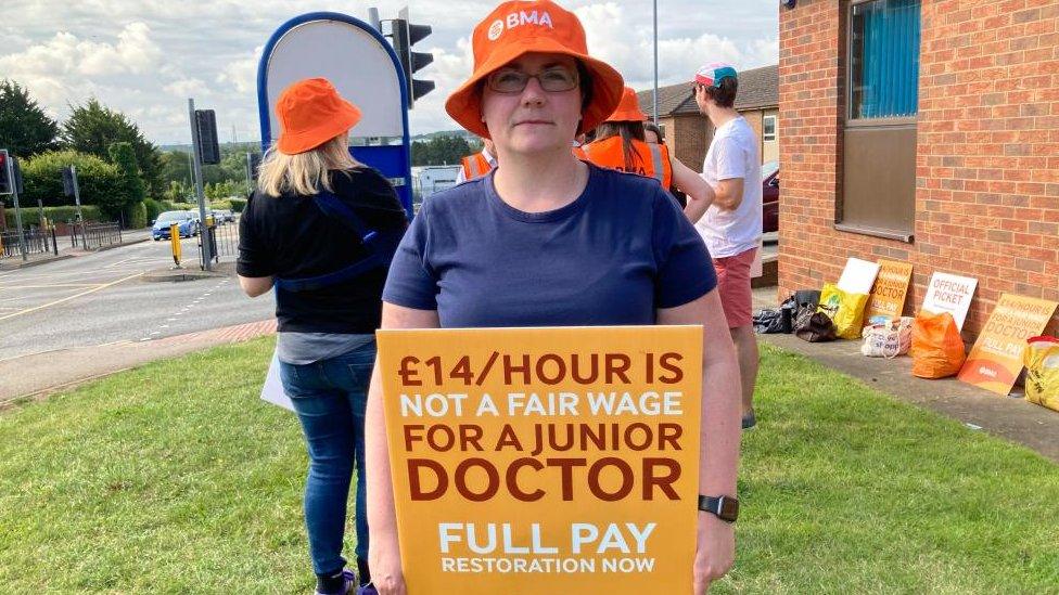 Woman wearing orange BMA hat and blue t-shirt, holding a "not a fair wage" placard