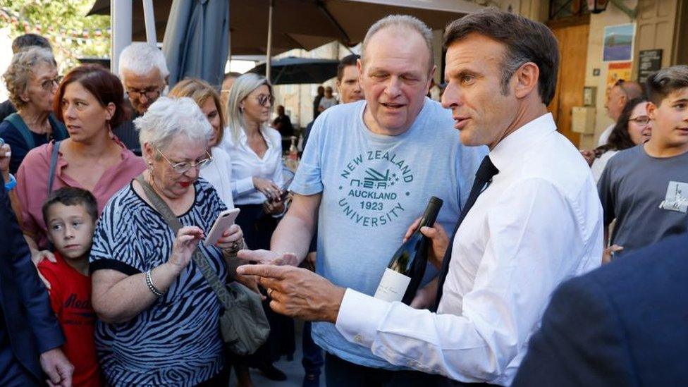 France's President Emmanuel Macron (R) is offered a bottle of wine as he meets residents of Baumes-de-Venise