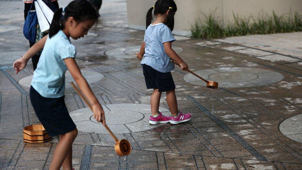 Japanese girls splash water on the ground during a water sprinkling event called Uchimizu which is meant to cool down the area, in Tokyo on July 23, 2018.