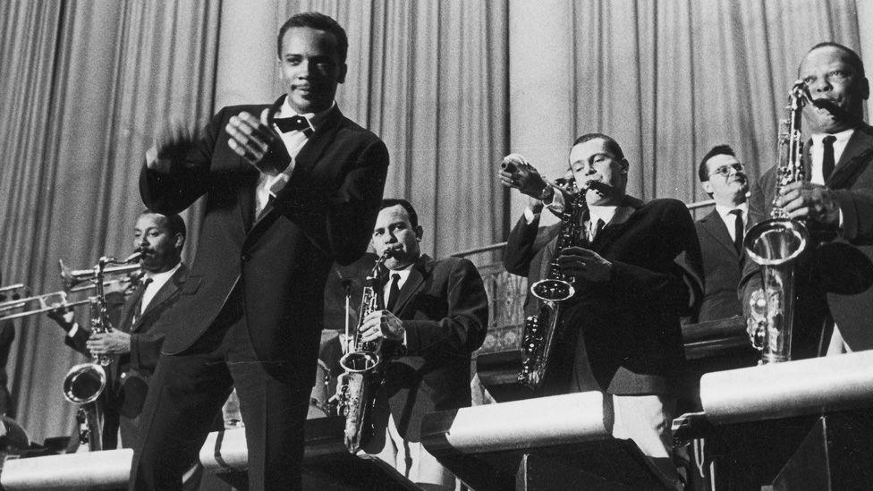 Quincy Jones clapping and dancing in front of musicians in his big band in about 1960