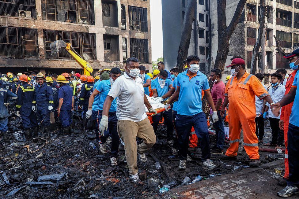 Rescuers wearing a variety of clothing - including fire officials - retrieve a body covered by a blanket, on a stretcher, from the ruins of the medical college on Thursday