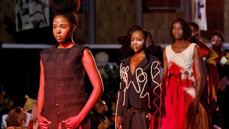 Several models walk up a catwalk mainly dress in black clothes with white face paint designs at the I Wear My Culture fashion show in Bulawayo, Zimbabwe - Saturday 30 August 2025.