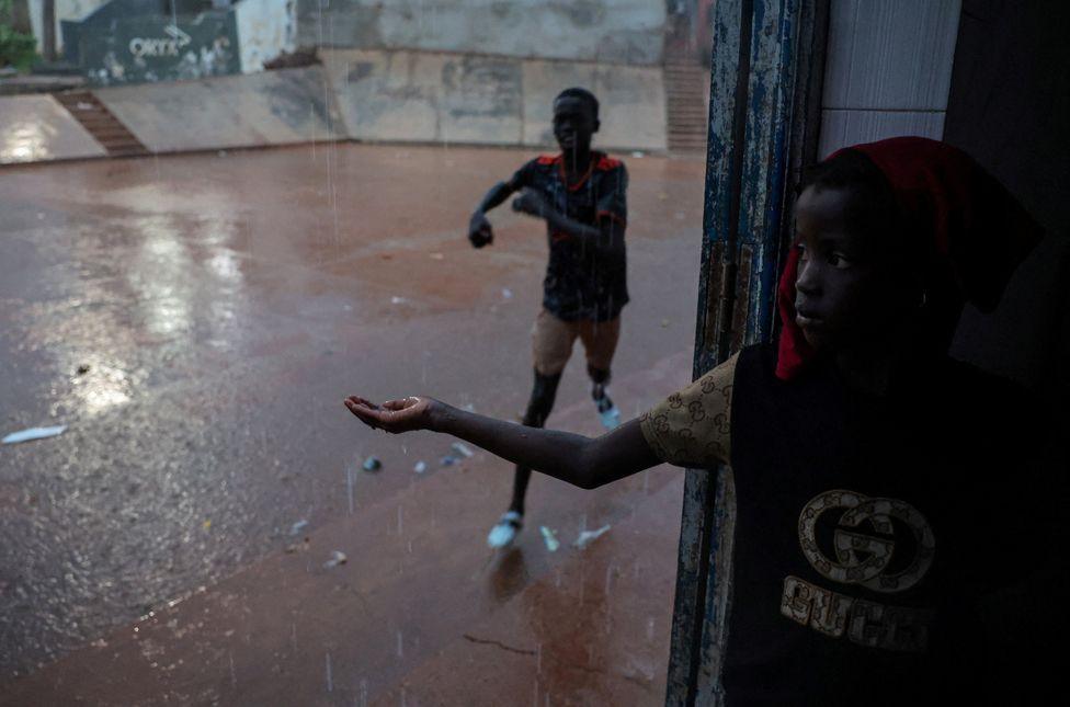 A girl looks on and a boy runs as it rains in Toubab Dialaw on the outskirts of Dakar, Senegal, 25 September 2024.