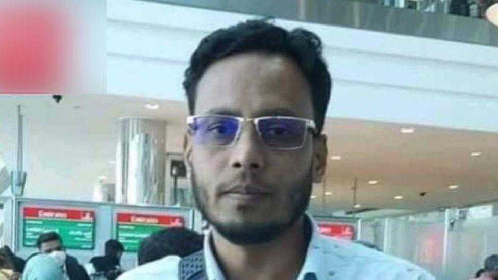 Mizanur Rahman, a man with dark hair, glasses and a beard wearing a blue shirt, standing in an airport