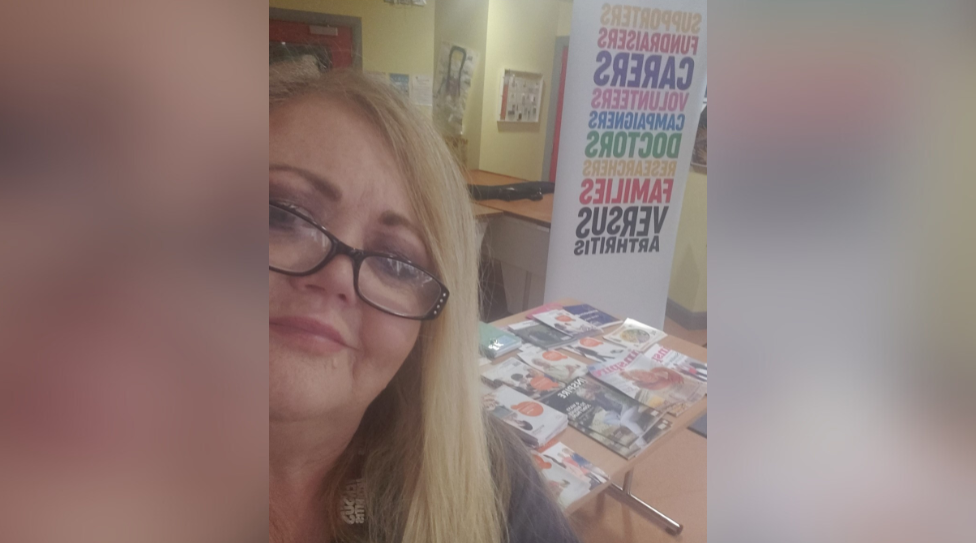 Tracey, a woman with blonde hair and glasses, at a Versus Arthritis information stand