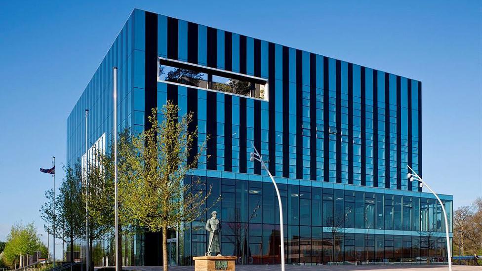 The exterior of Corby Cube - a large glass cube shaped building with many glass windows.