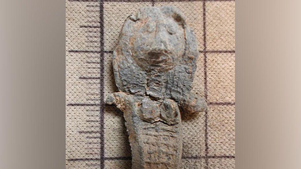 A close up picture of the medieval doll. Hair and eyes are easy to make out as well as short arms and breasts.