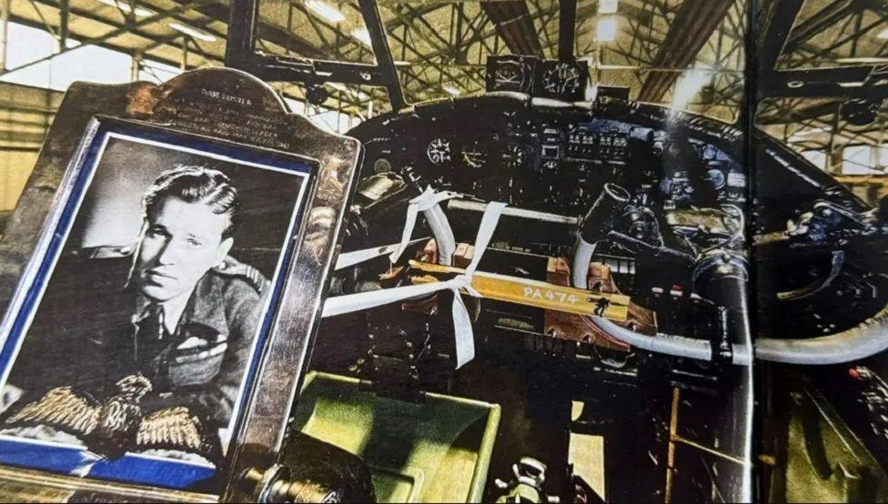 A framed picture of Guy Gibson with a pair of his cloth wings inset. The picture has been placed inside the cockpit of a Lancaster bomber