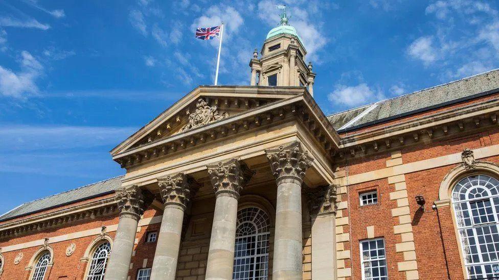 Front of Peterborough Town Hall, a red-brick building with four columns by the entrance and a union flag flying on the top