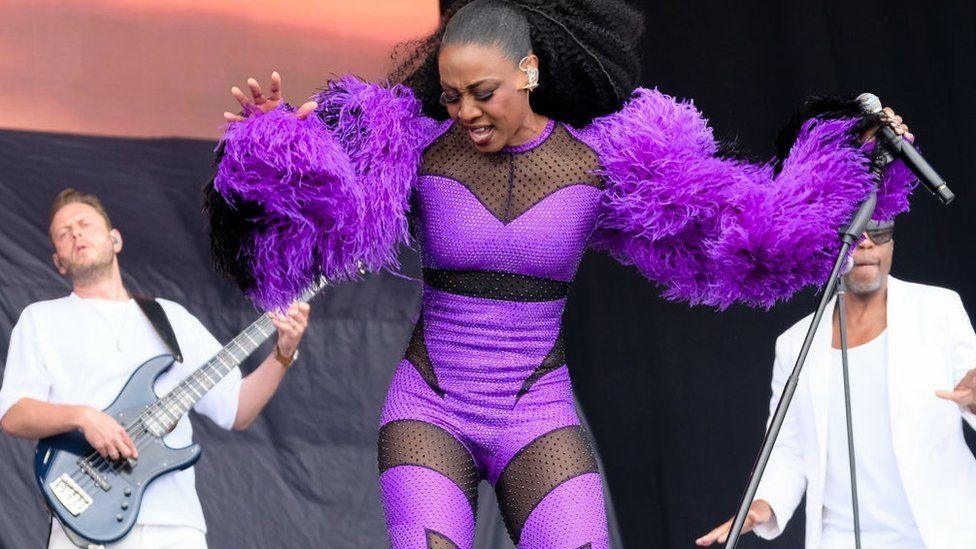 Beverly Knight in a bright purple and black bodysuit with purple feathered sleeves