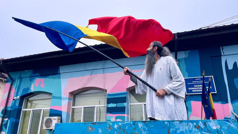 A bearded man waves a giant Romanian flag