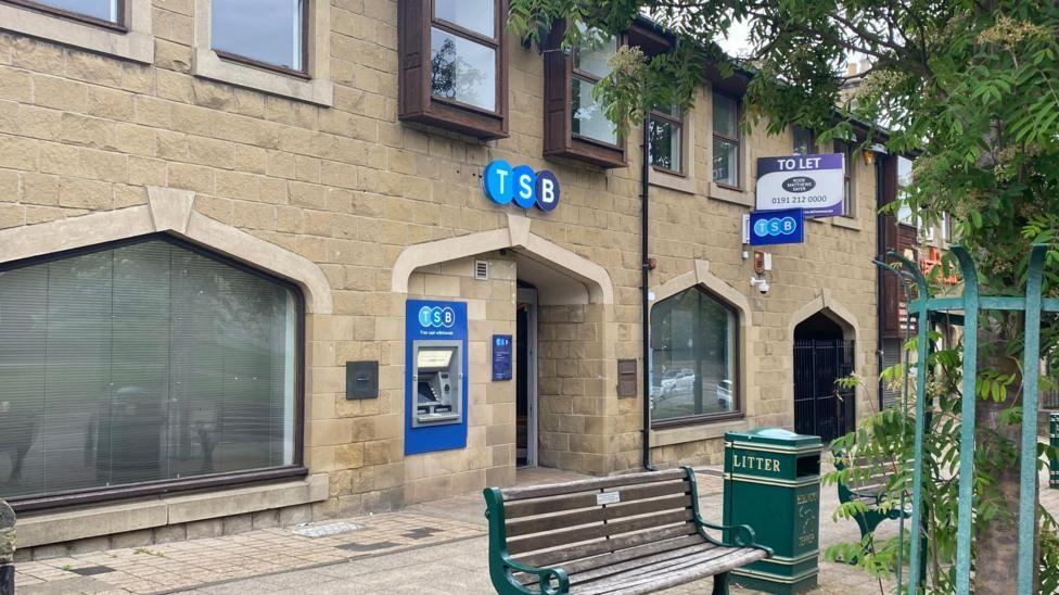 A branch of TSB with a seat and a green litter bin outside