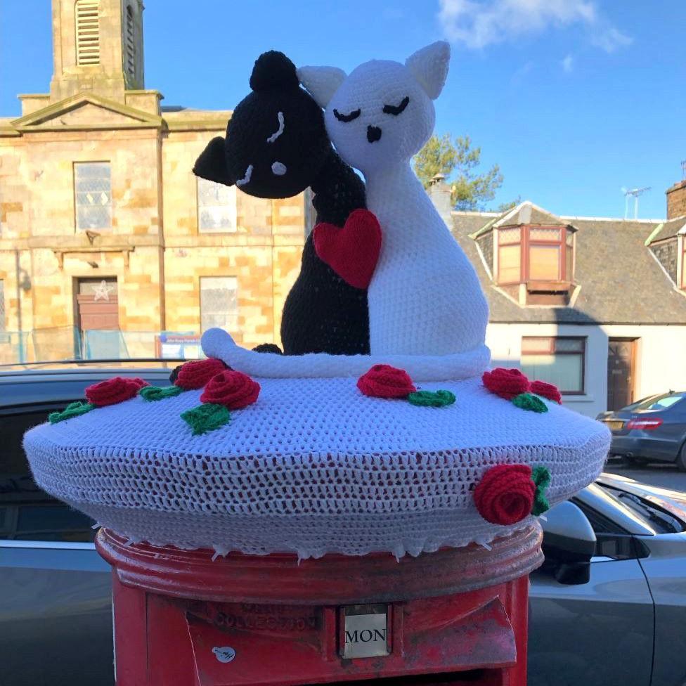 Knitted black and white cats with a red heart on top of a red post box.