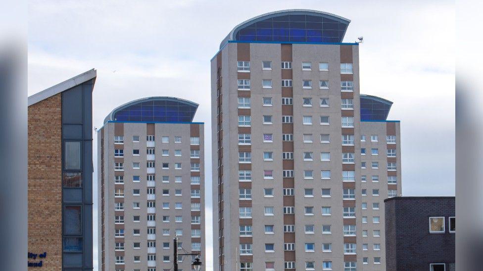 Lambton, Londonderry, and Lumley Towers in Sunderland's East End. There are three hi-rise blocks of flats that are beige-coloured with brown striped panels and a roof section that is blue-tinted. 
